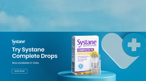 Image of a Systane lubricant eye drops box and vials on a blue pedestal. The background features a heart with a medical cross. Text reads: Systane. Try Systane Complete Drops. Now available in Vials. Shop Now.