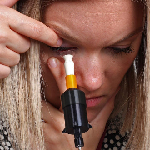 A person with light hair skillfully uses the S5 Inserter for Scleral & Hybrid Lens Insertion from Augmented Vision Labs, gently pulling down the eyelid and using hands-free stabilization techniques, demonstrating precise application. The product features adjustable height and comes with free video training.
