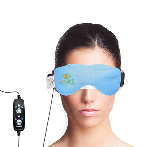 A person wears the OcuSci E-Compress USB Eye Heat Mask, featuring a blue washable cover and connected by a black cord to a multi-button remote. The brand name OcuSci is displayed on the mask as they enjoy therapeutic heat with their hair pulled back against a plain white background.