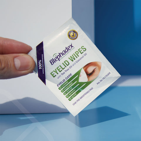 A hand presents Lunovus Blephadex Wipes 2-pack with tea tree and coconut oil. The packaging emphasizes eyelid care benefits with sleek icons on a calming blue-to-white gradient.