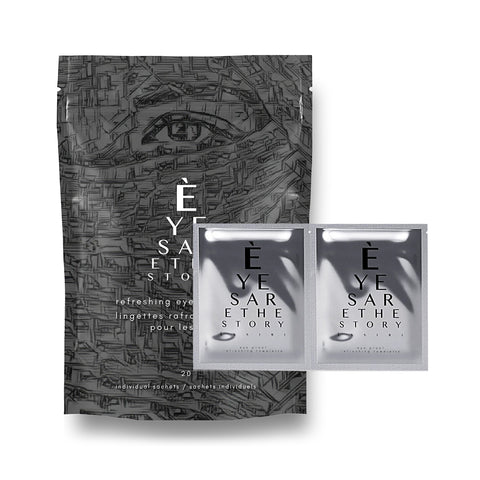A gray pack of Eyes are the Story Refreshing Towelettes Wipes for Eyelid Hygiene (20ct) features abstract line art and the text EYES ARE THE STORY. Two individual sachets exhibit a matching design and message.