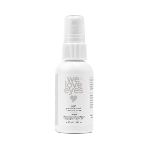 The 50mL We Love Eyes Calm Eyelid & Eyelash Cleansing Spray boasts a minimalistic white bottle with a spray nozzle, enriched with soothing chamomile and labeled in English and French, featuring a heart symbol for gentle cleansing.
