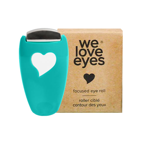 A turquoise eye roller with a heart cutout, made of stainless steel for best results, is next to a box labeled We Love Eyes - Focused Eye Roll: Tone, de-puff & relax tired eyes. Hot compress for massaging meibomian glands. Fingertip precision.