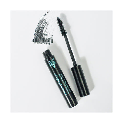 An open tube of We Love Eyes Lashfull Thinking BLACK Pressed Serum Mascara with Widelash lies next to a thick brushstroke on a white surface.