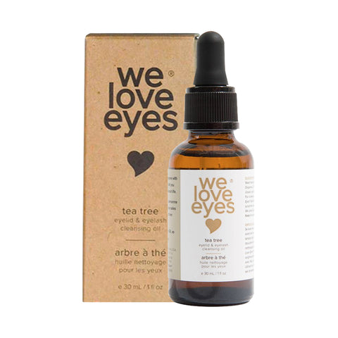 A brown glass We Love Eyes- All Natural Tea Tree Eyelid Cleansing Oil - 30ml bottle is elegantly placed next to a matching branded cardboard box with a heart symbol. The product, featuring tea tree and jojoba oils, is designed to cleanse Meibomian oil glands.