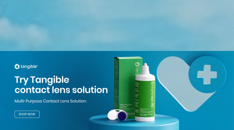 Contact lens solution promotional image featuring a green and white bottle beside its box, a contact lens case, and a blue heart with a medical cross icon. The text reads, Try Tangible contact lens solution. Multi-Purpose Contact Lens Solution. Shop Now.