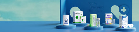 A display of eye care products on blue platforms, including contact lens solutions, eye drops, and care kits. The background features a blue board with a cut-out cross symbol and the text “Daily Eye Care. Simplified.”.