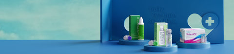 A display with contact lens solutions and eye care products on blue platforms. Boxes and bottles are neatly arranged against a blue backdrop with the text Daily Eye Care Simplified and a medical cross symbol. A soft green gradient background.