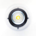 An overhead shot captures the S5 Mini Inserter by Augmented Vision Labs, resembling a small, round container with a yellow interior. It sits centrally on a larger circular black and white backdrop, giving the image an abstract feel with soft focus. Free video training is included.