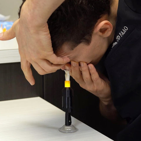 A person uses the S5 Mini Inserter for Scleral & Hybrid Lens Insertion by Augmented Vision Labs, aligning their eye and supporting their forehead. They demonstrate precise technique with the help of free video training included with the device for effective lens insertion.
