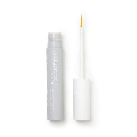 A gray tube of Daily Practice Lash Enhancing Serum, enriched with biomimetic peptides, has a white cap and yellow-tipped brush applicator. Positioned on a white background, its sleek design embodies innovative beauty solutions for fuller, longer, healthier lashes.