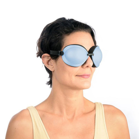 A woman with short dark hair wears a beige tank top and large light blue EyeEco Tranquileyes XL goggles—advanced moist-heat & cold therapy eyewear for severe dry eye and MGD—facing slightly right against a plain white background.