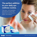 A woman uses Bruder Hygienic Eyelid Cleansing Wipes on her eyelids while looking into a mirror. The text highlights the wipes as ideal for daily eye wellness and dry eye relief by removing oil, debris, and makeup. A box of 30 pre-moistened wipes is shown in the corner, promoting ocular health.