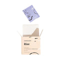 An open box of CorneaCare Wipes with Tea Tree Oil (30ct) reveals a packet gently rising. The minimalist design in light hues and abstract patterns hints at the soothing power within, enriched with tea tree oil for effective eyelid cleansing by CorneaCare.