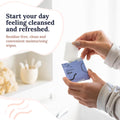 In a bright bathroom, someone pulls a CorneaCare Wipe with Tea Tree Oil from the box. The label reads: Start your day feeling cleansed and refreshed. Residue-free, clean and convenient moisturizing wipes.
