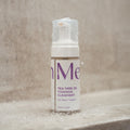 The Merakim Tea Tree Oil Foam Facial Cleanser (120mL) sits on a wet surface, glistening with droplets that evoke a refreshing shower scene. The label highlights its soothing benefits for face and eyelids, especially helpful for those with ocular inflammation.