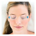 A relaxed woman with her eyes closed lies on a white surface, benefiting from dry eye relief. Her long hair is pulled back, and she wears clear SleepTite, SleepRite daily nighttime lid closure devices by Ophthalmic Resources Partners, featuring blue squares near the temples.