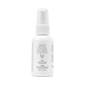 The 50mL We Love Eyes Calm Eyelid & Eyelash Cleansing Spray boasts a minimalistic white bottle with a spray nozzle, enriched with soothing chamomile and labeled in English and French, featuring a heart symbol for gentle cleansing.