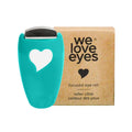 A turquoise eye roller with a heart cutout, made of stainless steel for best results, is next to a box labeled We Love Eyes - Focused Eye Roll: Tone, de-puff & relax tired eyes. Hot compress for massaging meibomian glands. Fingertip precision.