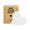 A cardboard box labeled We Love Eyes with a heart symbol contains the We Love Eyes Eyelid Scrub Mitt and a textured, heart-shaped white pad.