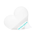 A heart-shaped white object resembling an eyelid scrub mitt has a slight crease down the middle. A small label on the bottom right reads We Love Eyes in teal, next to a teal heart. The plain white background highlights eye care essentials.