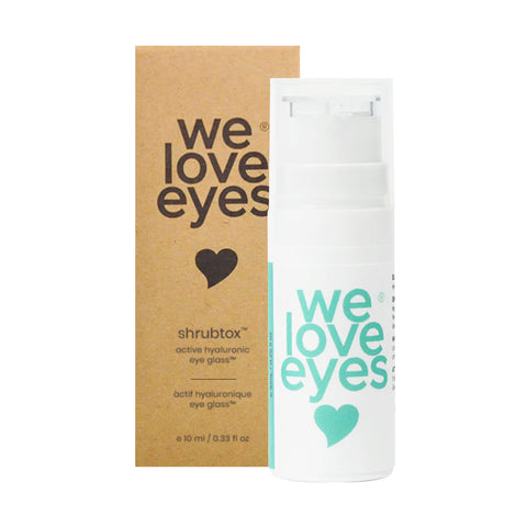 A white pump bottle of We Love Eyes Shrubtox Active Hyaluronic Eye Glass stands next to its box, both featuring a heart graphic. It promises to care for your eyelid skin barrier with active hyaluronic acid, helping reduce fine lines and wrinkles.