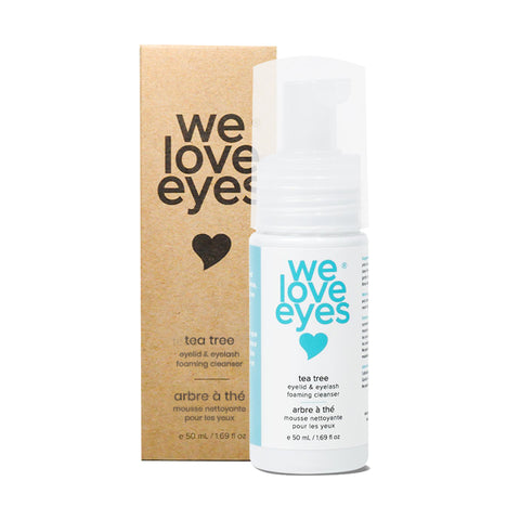 The We Love Eyes Tea Tree Eyelid & Eyelash Foaming Cleanser 25mL Mini Size sits elegantly beside its coordinating cardboard box, featuring a heart design with blue and black text. The bottle is equipped with a clear pump dispenser for convenient use.