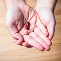 Hands gently hold a red pill over wood, reflecting EyePromise DVS Eye Vitamins dedication to retinal support.